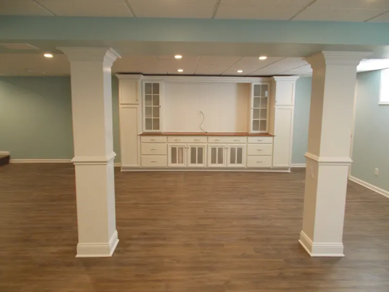 Finished basement with wrapped columns and a white built-in wall unit