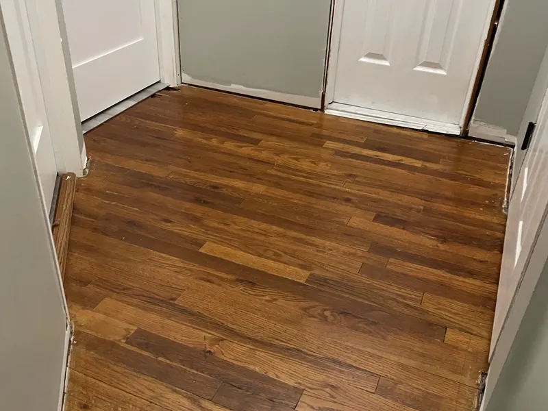 Refinished oak hardwood floor in a hallway between two white doors
