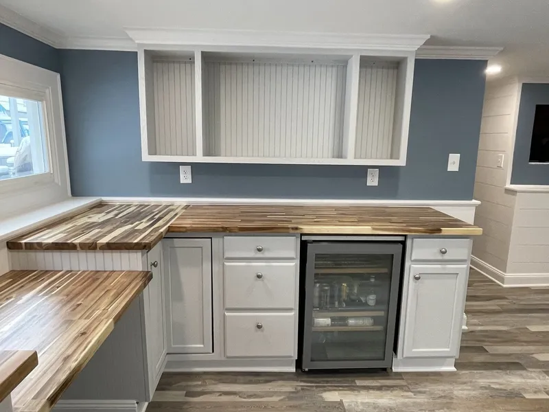 Finished basement bar with white shaker cabinets, butcher block counters, and a wine fridge